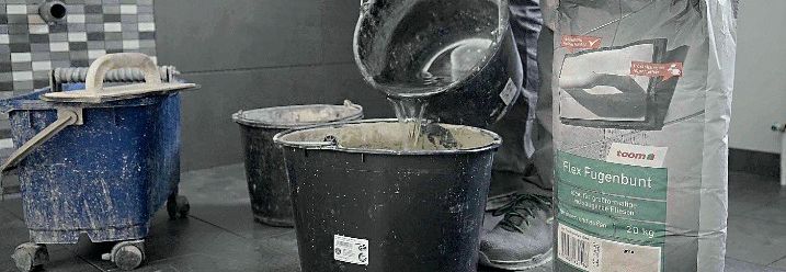 Ein Handwerker gibt Wasser in einen großen Eimer mit Fugenmörtel.